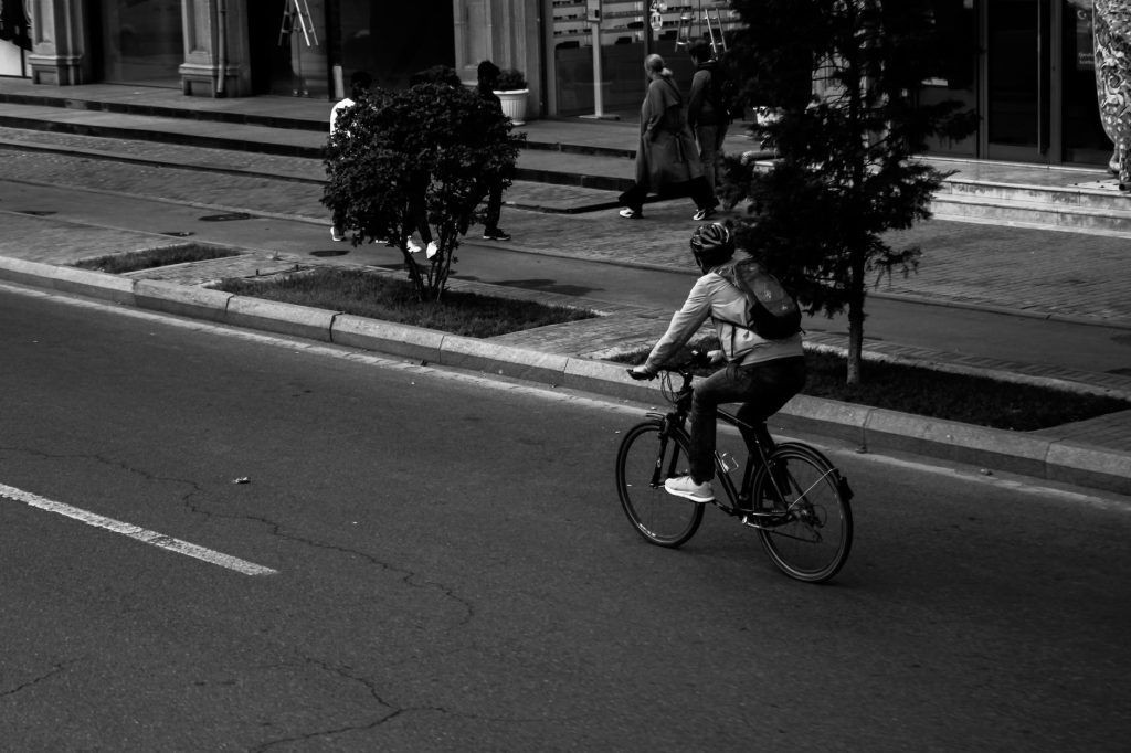 grayscale photo of man riding bicycle on road